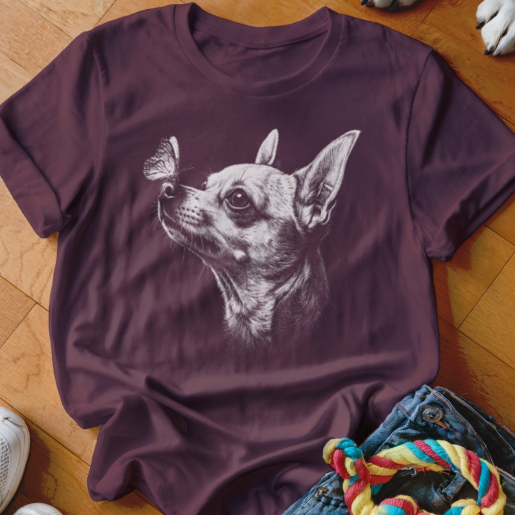 A dark purple t-shirt features a white sketch of a Chihuahua looking at a butterfly on its nose.