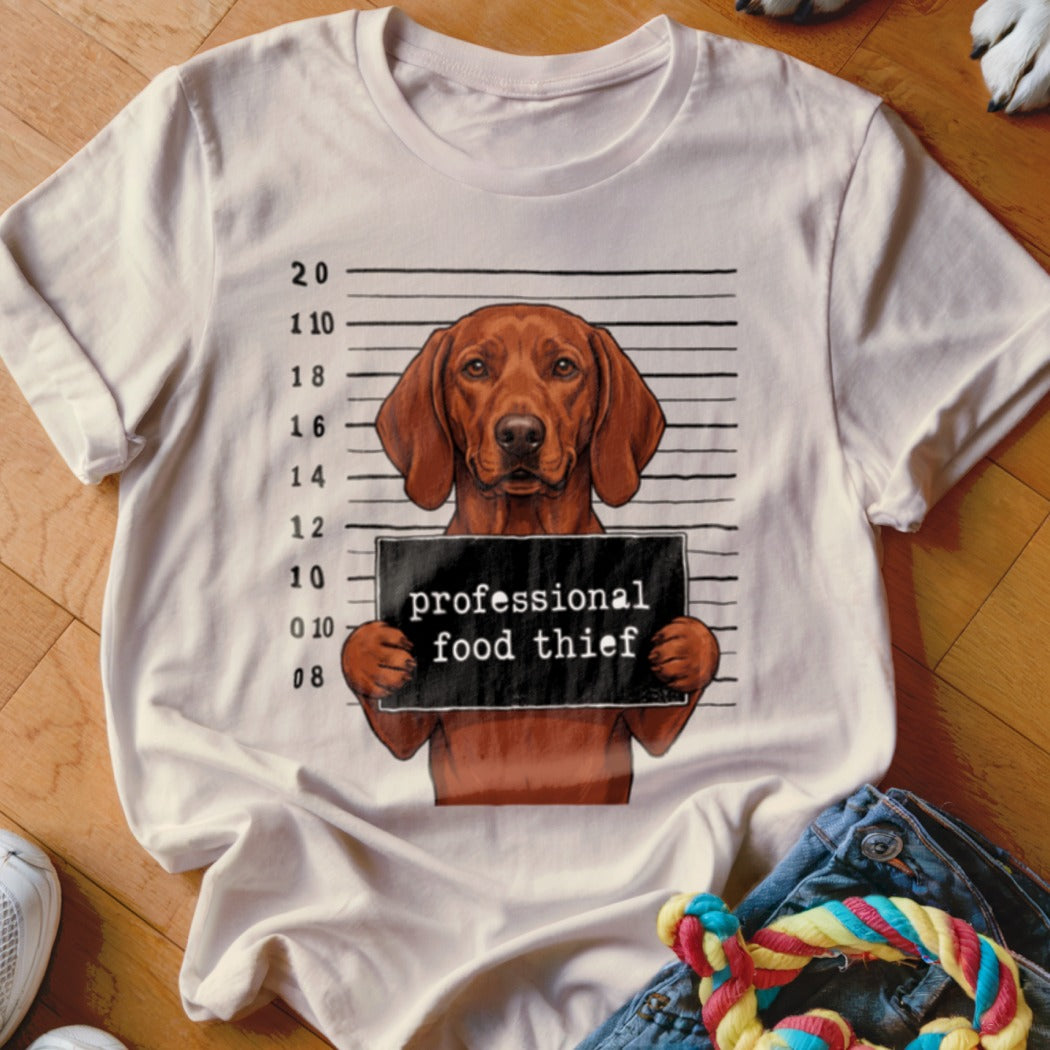 Brown dog wearing a mugshot sign that reads "professional food thief".