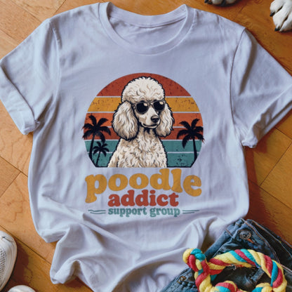 A white t-shirt featuring a retro graphic of a poodle in sunglasses with palm trees and sunset stripes.