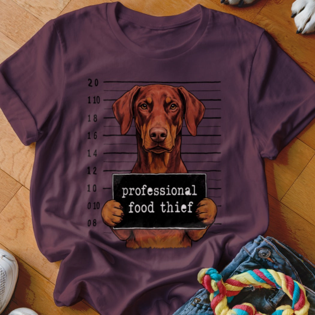 Brown dog in mugshot holding "professional food thief" sign.