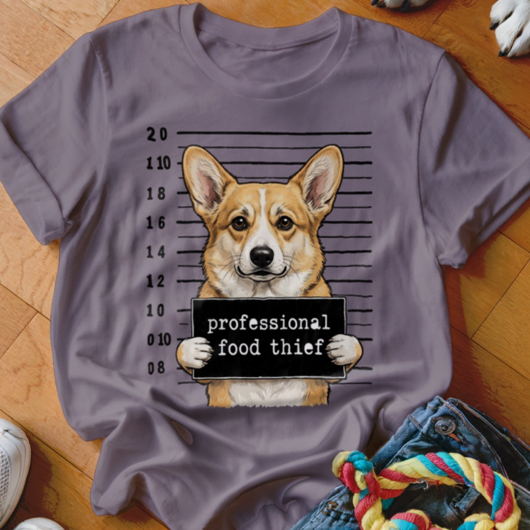 Corgi dog in mugshot holding a "professional food thief" sign on a purple t-shirt.