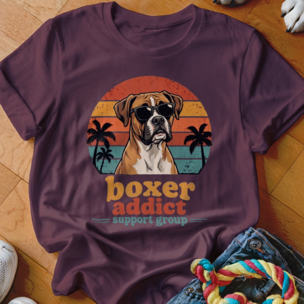 Plum-colored t-shirt featuring a retro sunset graphic of a Boxer dog wearing sunglasses, with palm trees and text reading boxer addict support group.