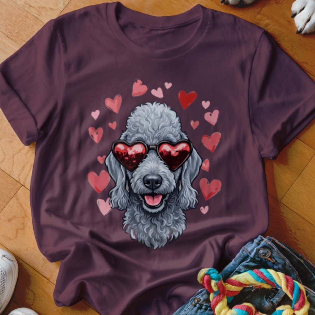 A dark purple t-shirt features a graphic of a grey poodle wearing heart-shaped sunglasses surrounded by floating pink hearts.