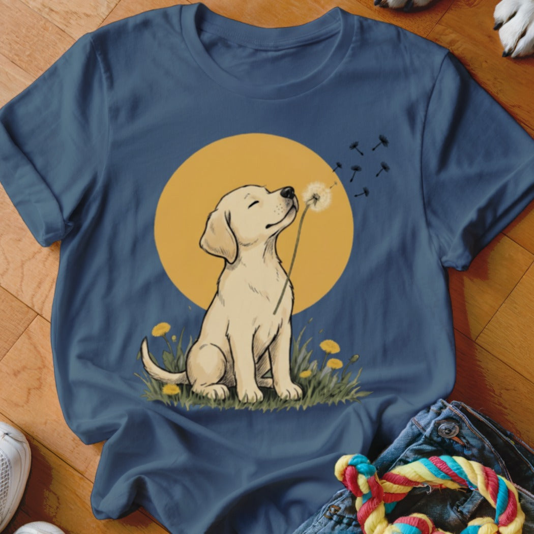 A blue t-shirt printed with a graphic of a yellow lab puppy blowing dandelion seeds.