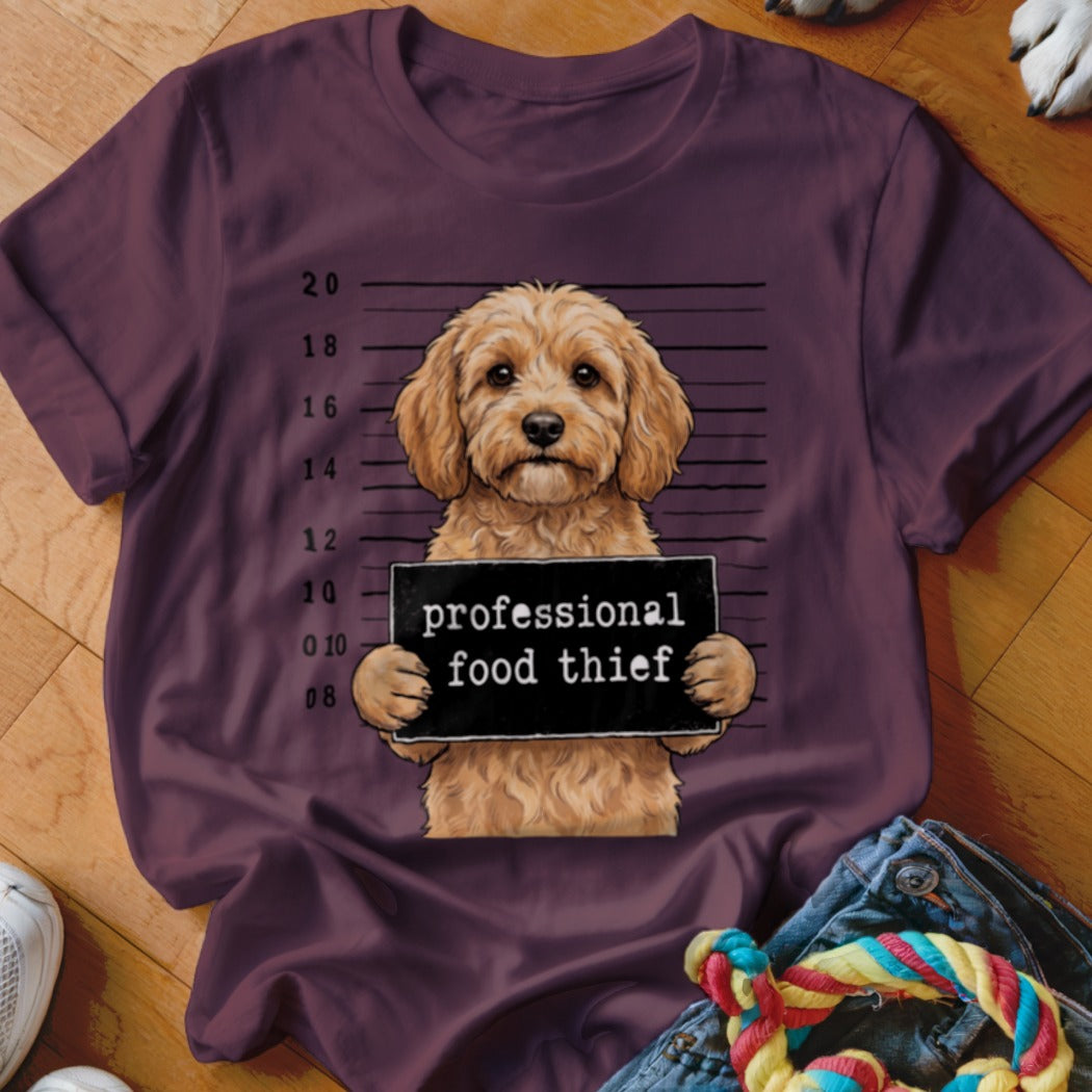 Fluffy dog mugshot holding "professional food thief" sign on plum t-shirt