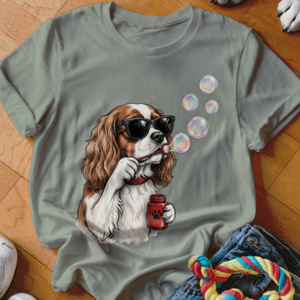 Sage green t-shirt featuring a graphic of a Cavalier King Charles Spaniel wearing sunglasses and blowing bubbles.