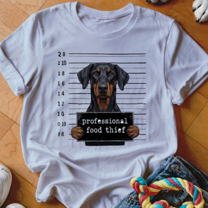 Doberman dog mugshot with "professional food thief" sign on white t-shirt.