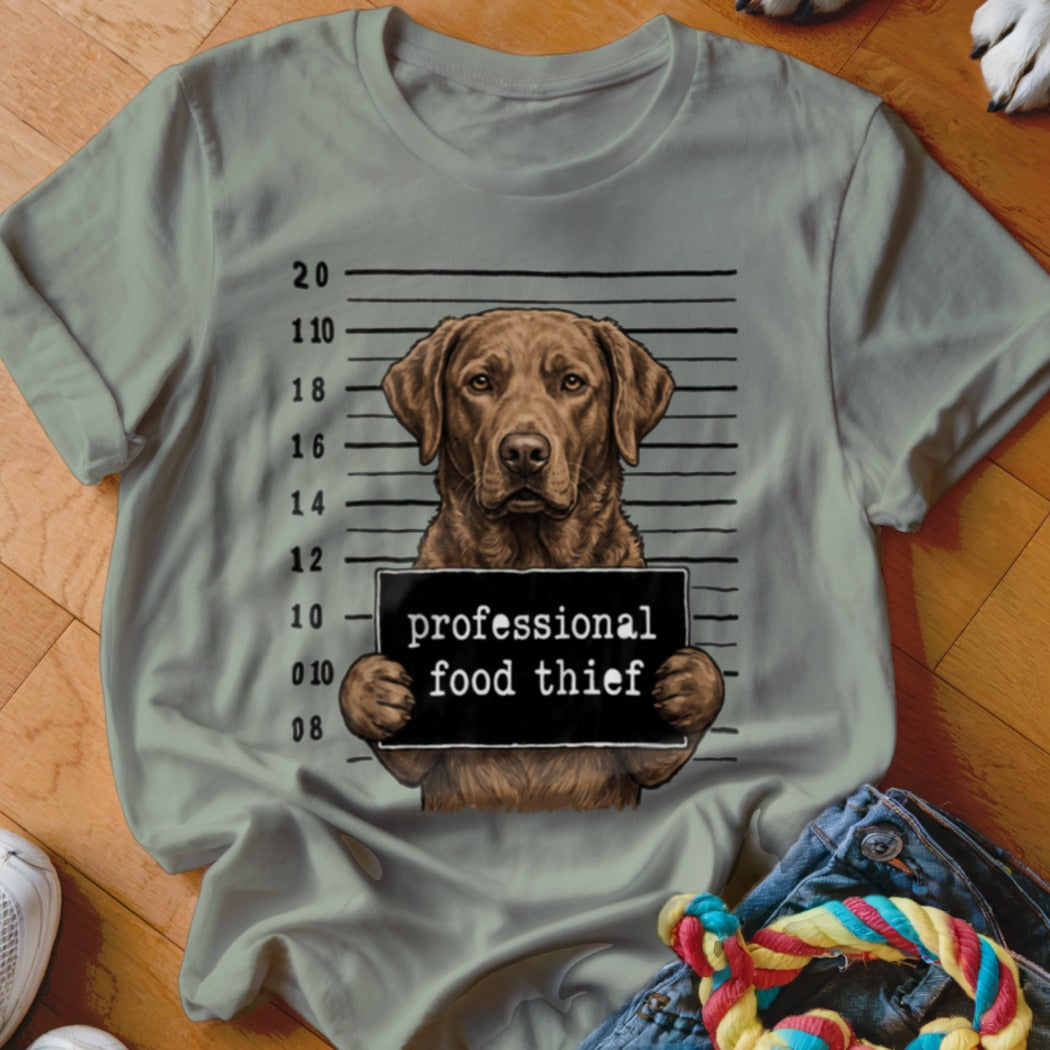 Brown dog mugshot with "professional food thief" sign on a light green t-shirt.