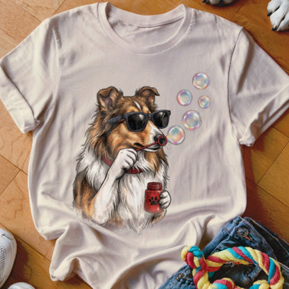 A cream-colored t-shirt with a graphic of a Shetland Sheepdog wearing sunglasses and blowing bubbles.