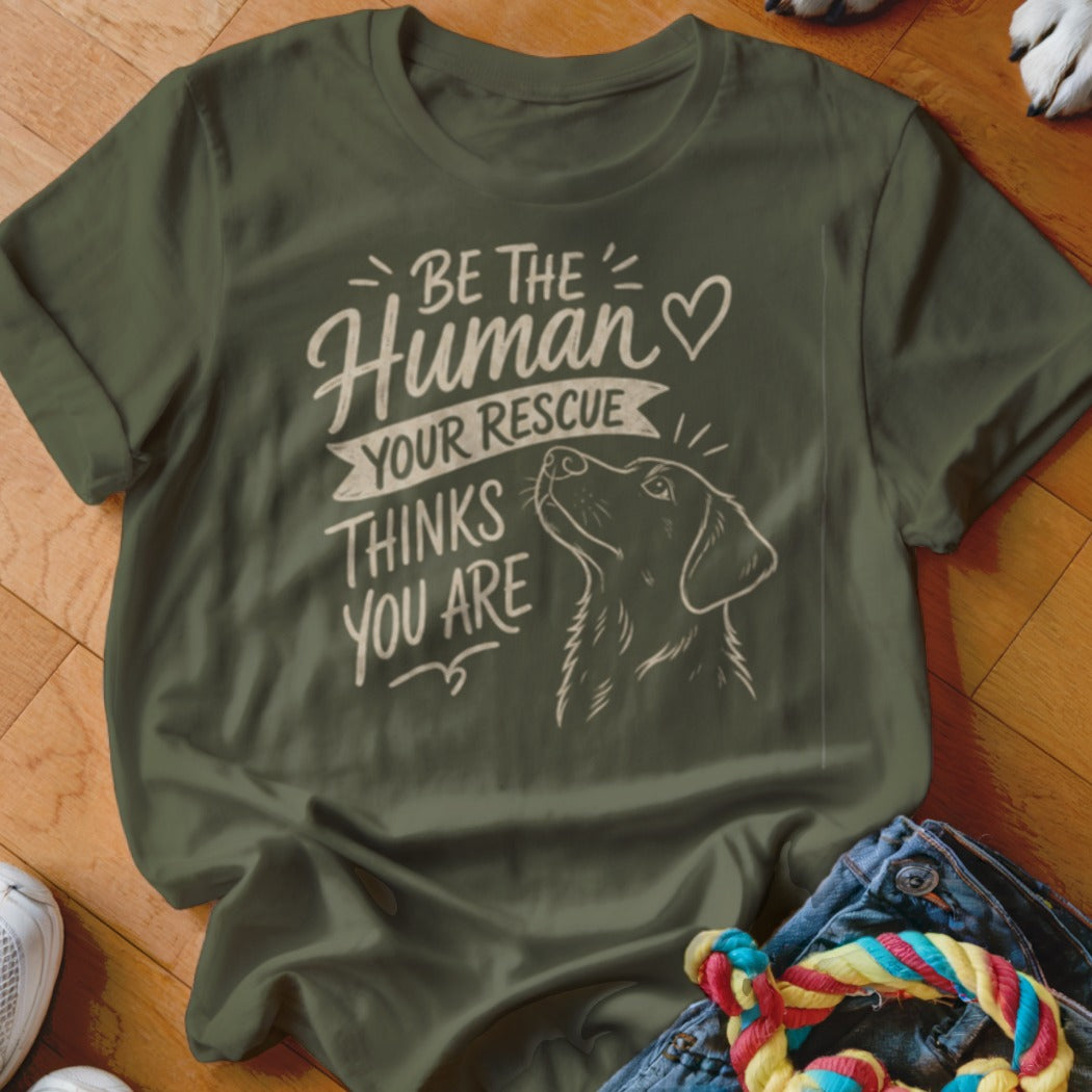 Olive green t-shirt with dog illustration and text "BE THE HUMAN YOUR RESCUE THINKS YOU ARE".