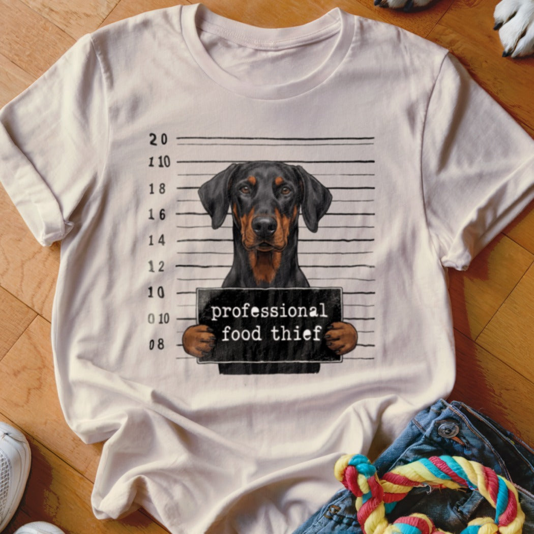 Doberman mugshot with "professional food thief" sign on a t-shirt.