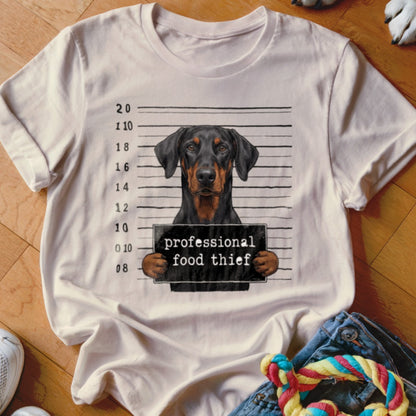 Doberman mugshot with "professional food thief" sign on a t-shirt.