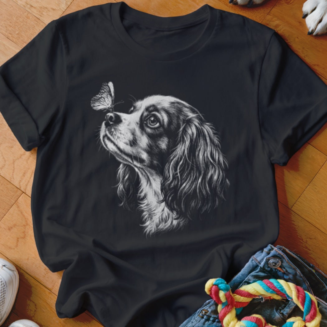 A black t-shirt featuring a white sketch graphic of a spaniel looking at a butterfly.