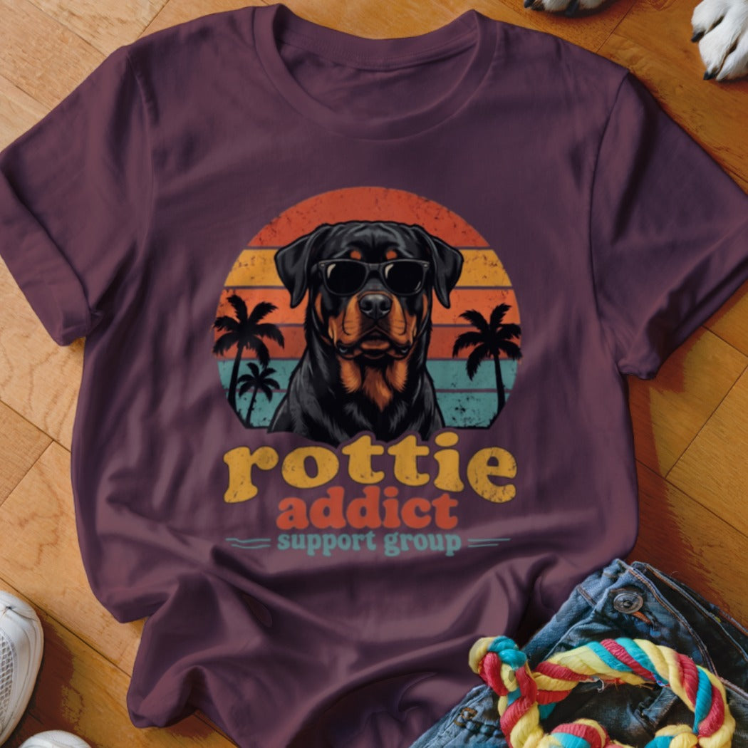 Maroon t-shirt featuring a retro graphic of a Rottweiler wearing sunglasses, palm trees, and text reading Rottie Addict Support Group.