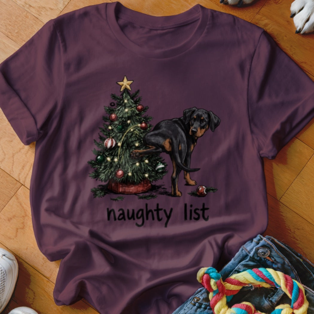 Rottweiler near Christmas tree with "naughty list" text printed on burgundy t-shirt.