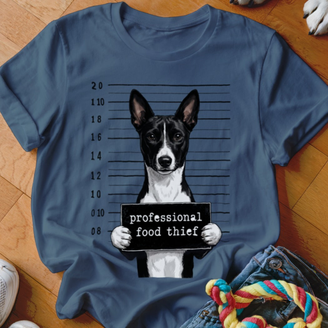 Basenji dog with "professional food thief" sign in mugshot background.