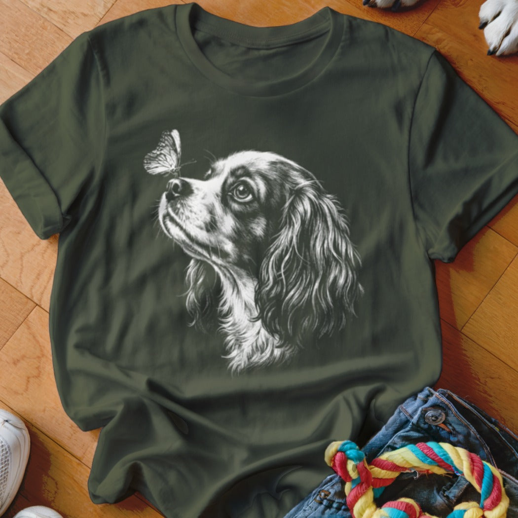 Dark green t-shirt featuring a white graphic print of a Cavalier King Charles Spaniel looking at a butterfly.