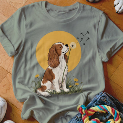 Sage green crewneck t-shirt featuring a cartoon spaniel blowing dandelion seeds in front of a yellow sun.