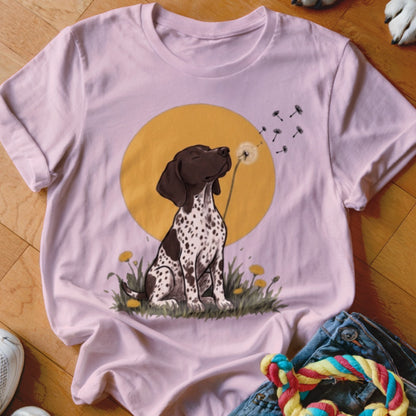A pink short-sleeve t-shirt featuring a graphic of a spotted dog blowing a dandelion.