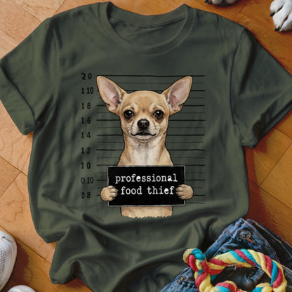 Chihuahua mugshot with "professional food thief" sign on dark green shirt.