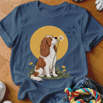 Navy blue t-shirt featuring a cartoon Cavalier King Charles Spaniel blowing dandelion seeds in front of a yellow sun.