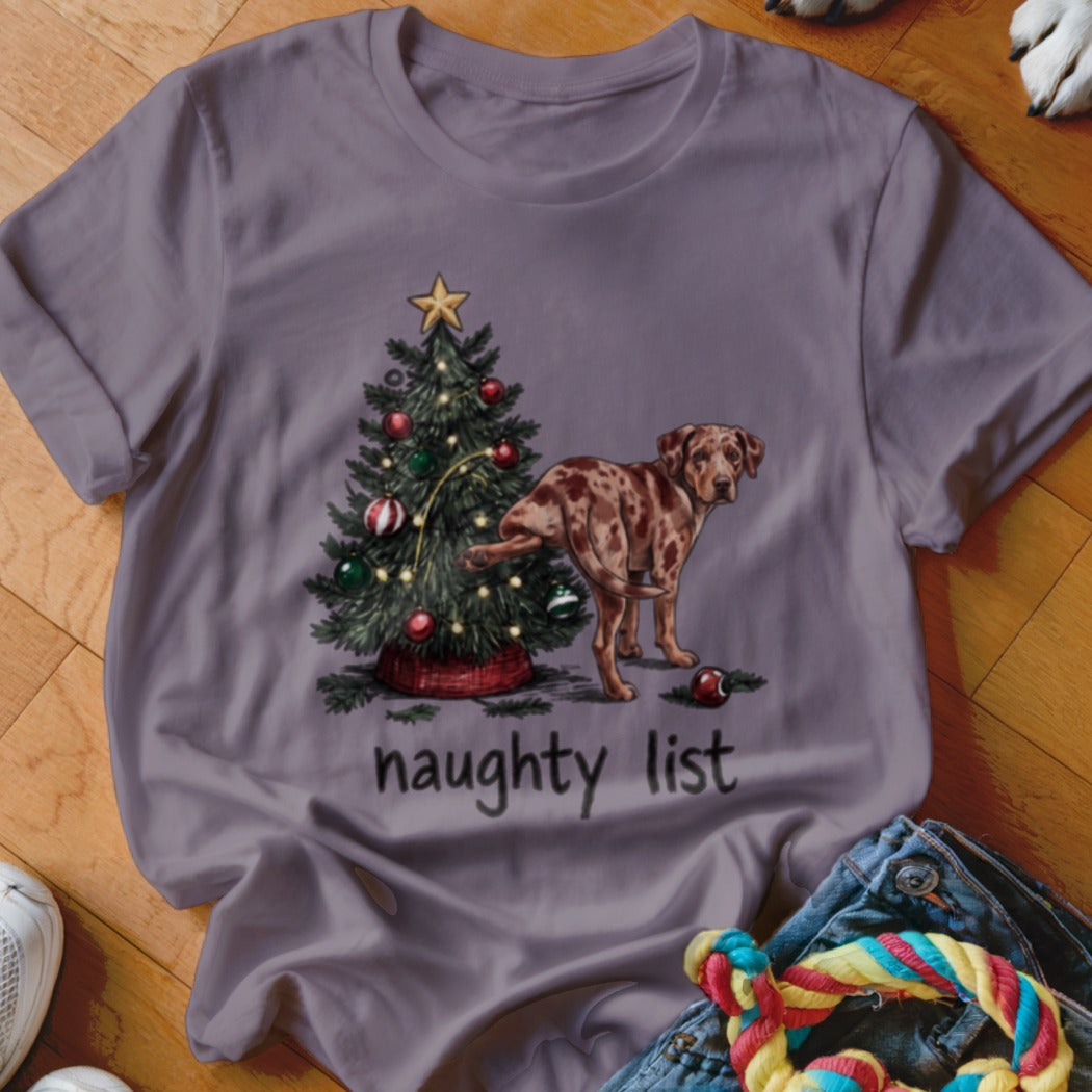 A grey t-shirt featuring a graphic of a spotted dog peeing on a Christmas tree with the words naughty list beneath it.