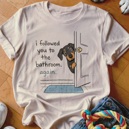 Cream t-shirt with cartoon dog peeking from a doorway, text says "I followed you to the bathroom. Again."