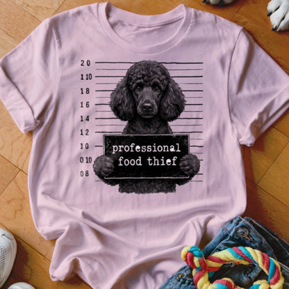 Light pink t-shirt graphic of a black poodle in a mugshot with "professional food thief" sign.