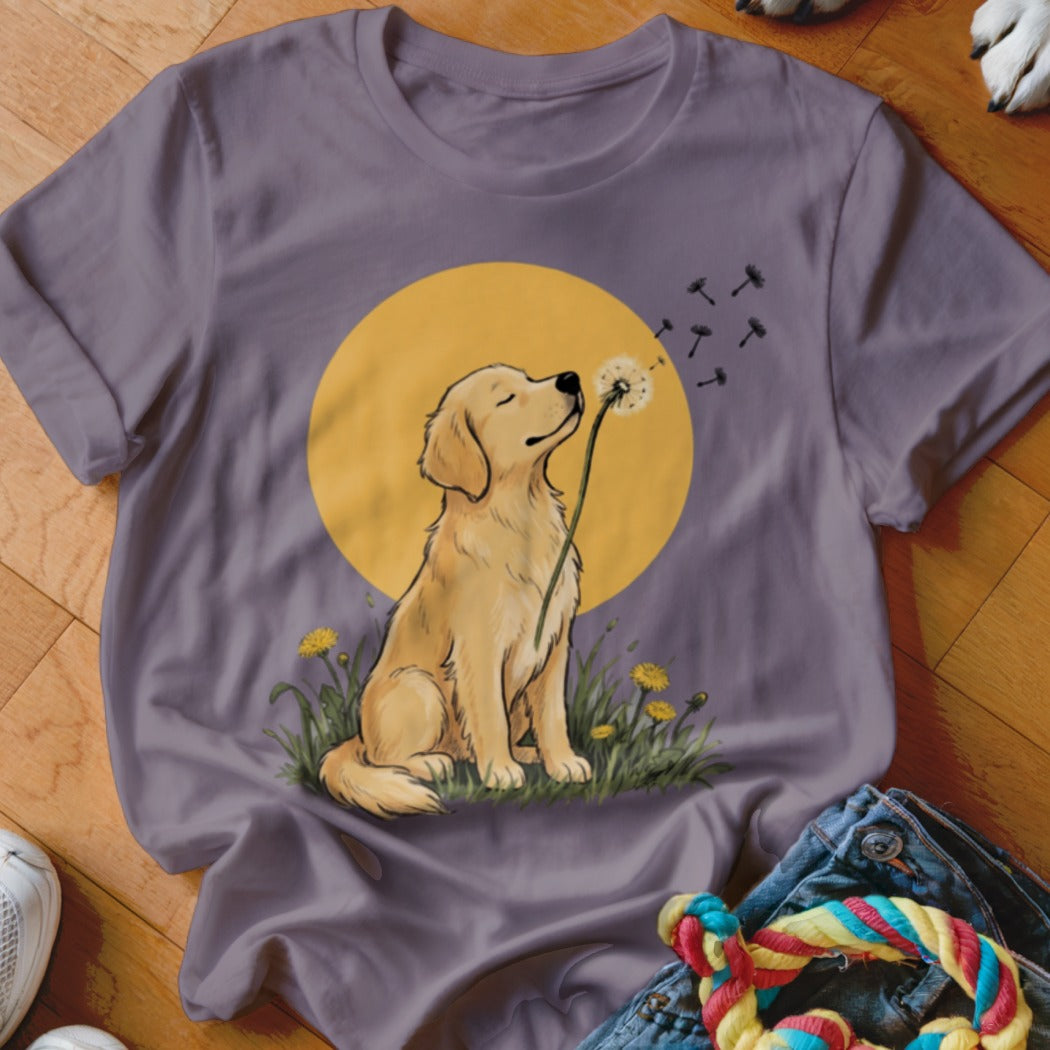 A purple t-shirt featuring a graphic of a golden retriever blowing dandelion seeds against a yellow sun.