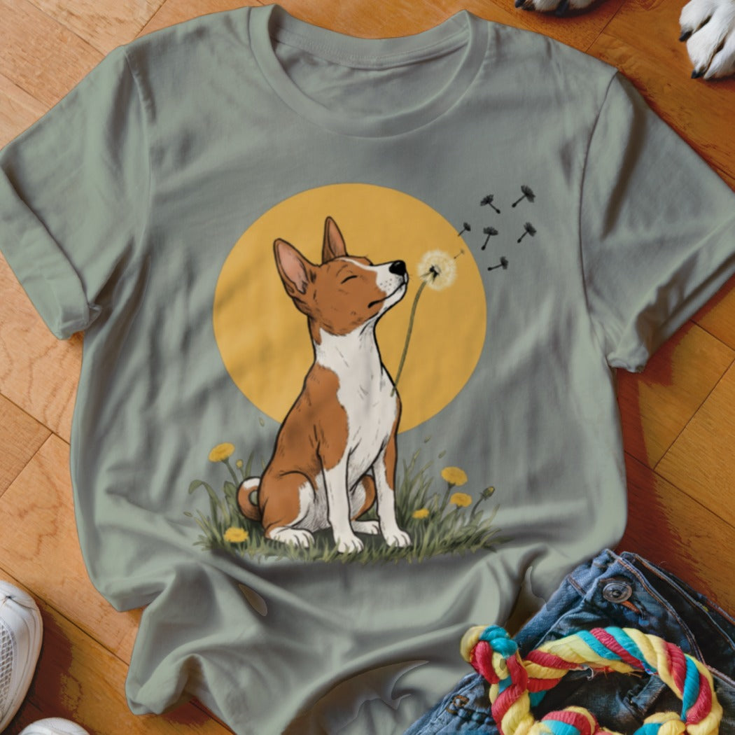 Sage green t-shirt featuring an illustration of a brown and white dog blowing dandelion seeds.