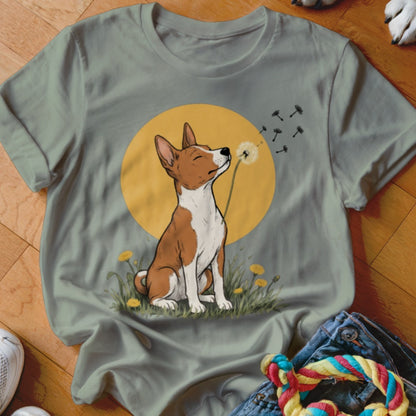 Sage green t-shirt featuring an illustration of a brown and white dog blowing dandelion seeds.