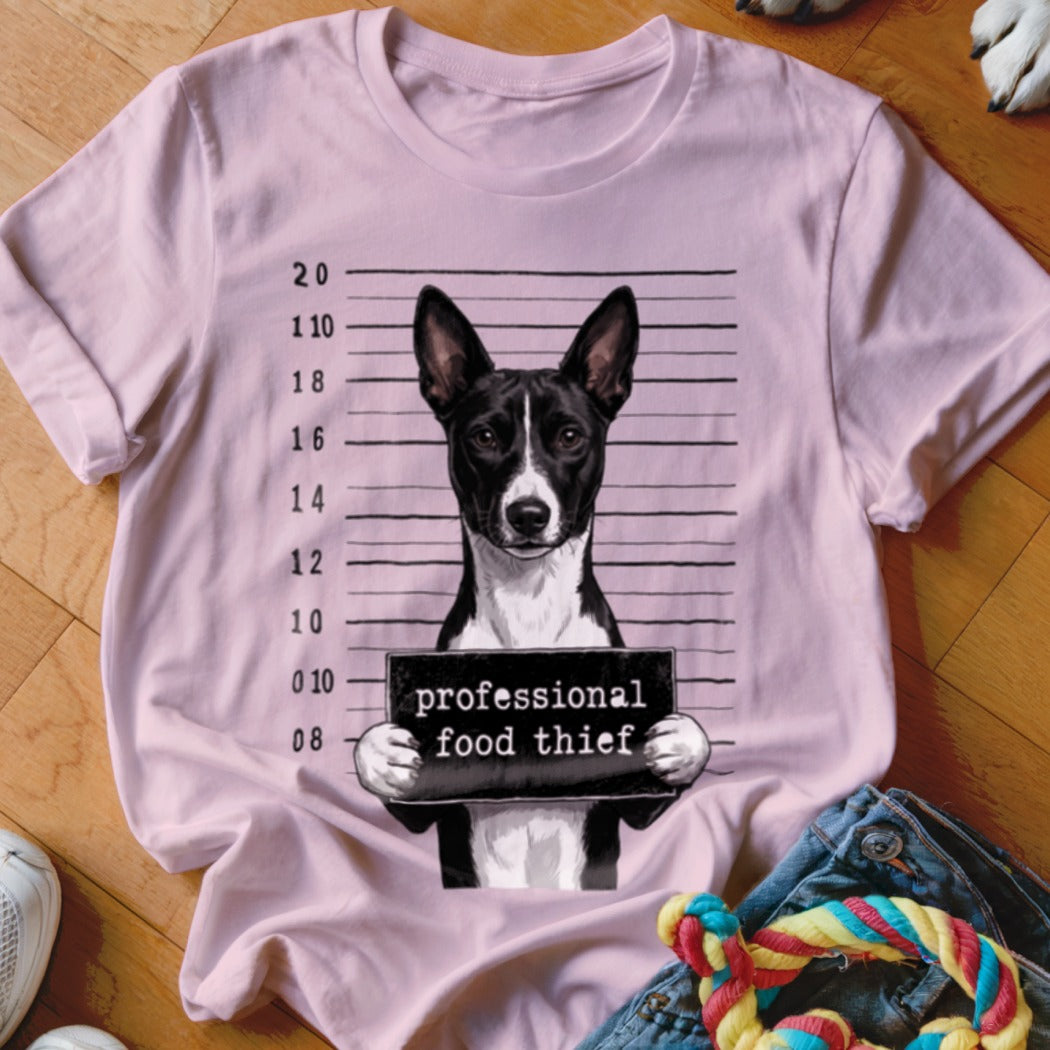 Dog in mugshot holding "professional food thief" sign on a pink t-shirt.