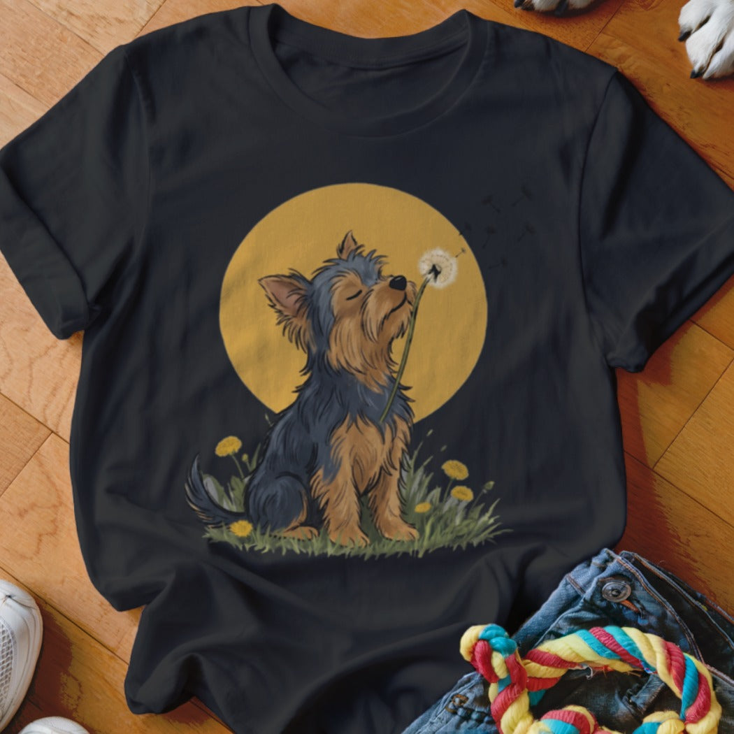 A black t-shirt printed with a Yorkshire terrier blowing dandelion seeds against a yellow moon.