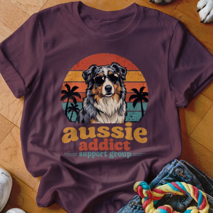 A dark purple t-shirt featuring a retro graphic of an Australian Shepherd wearing sunglasses against a sunset.