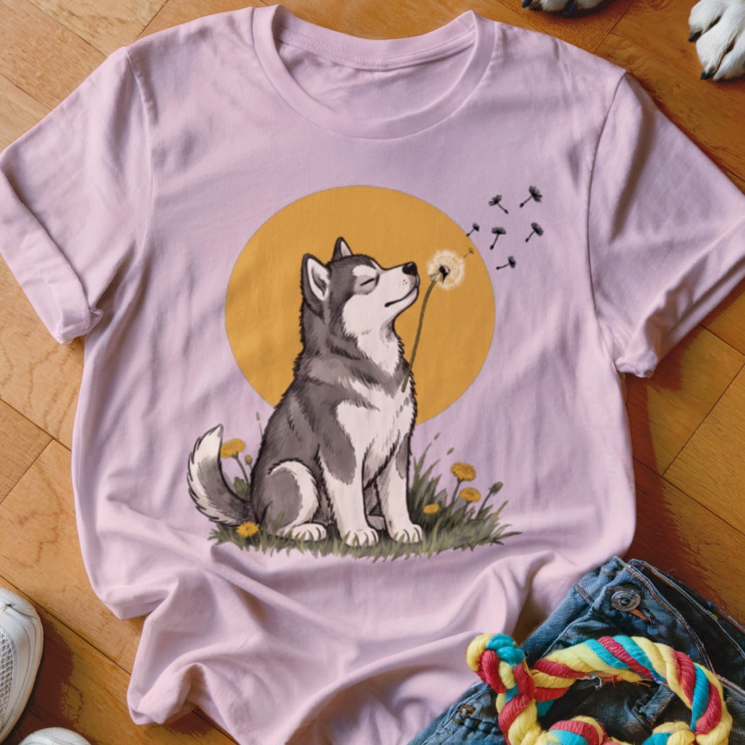 A light pink t-shirt featuring a graphic of a husky blowing dandelion seeds against a yellow circle background.