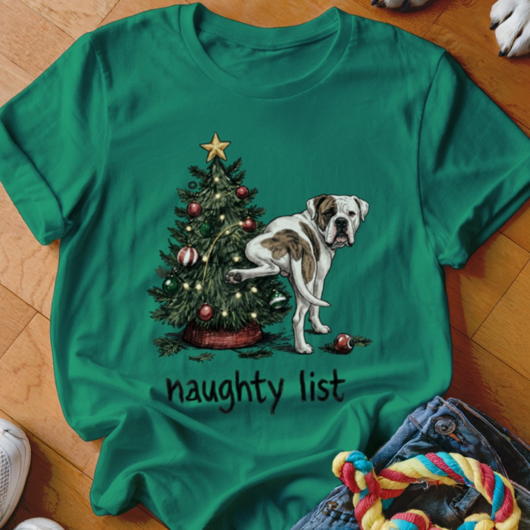 American Bulldog by Christmas tree with "naughty list" text on green t-shirt.