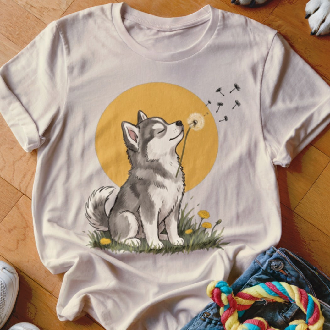 A cream-colored t-shirt with a graphic of a husky puppy blowing a dandelion against a yellow circle background.