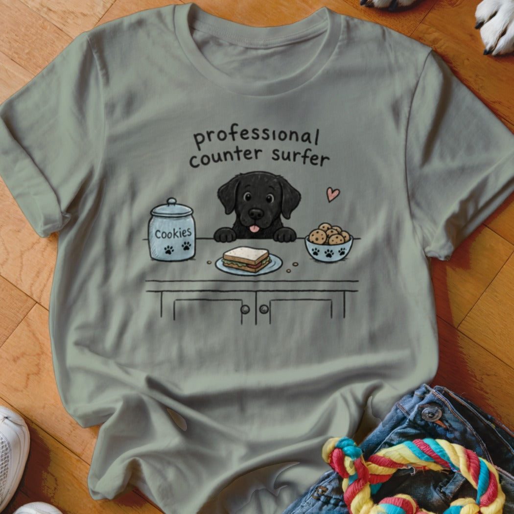 Black Labrador puppy looking at a sandwich and cookies with "professional counter surfer" text.