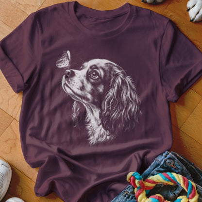 A dark purple short-sleeved t-shirt features a white sketch of a King Charles Spaniel looking at a butterfly.