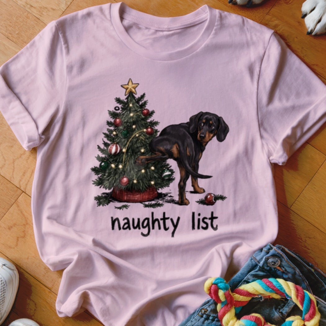 Pink t-shirt with a dog near a Christmas tree and the words "naughty list".