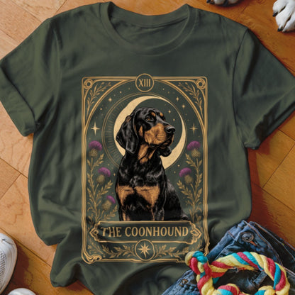 Dark green t-shirt featuring a tarot card style graphic of a black and tan coonhound surrounded by purple thistles and a crescent moon.