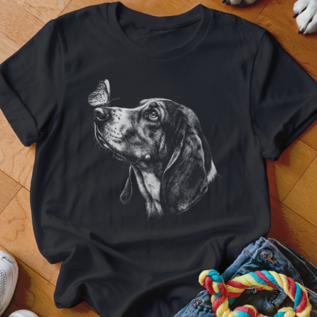 A black t-shirt features a white sketch of a dog looking at a butterfly on its nose.