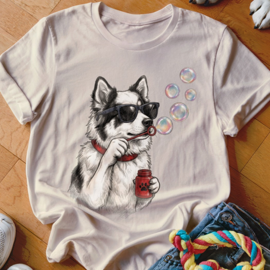 A light-colored t-shirt featuring a graphic of a black and white dog wearing sunglasses and blowing bubbles.