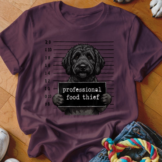 Black dog mugshot with "professional food thief" sign on maroon t-shirt.