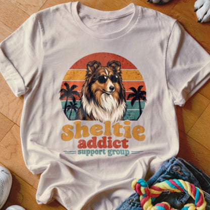 Off-white t-shirt featuring a retro graphic of a Sheltie in sunglasses against a sunset.