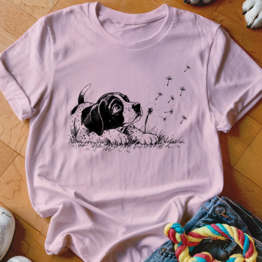 Pink t-shirt featuring a black and white graphic of a puppy watching dandelion seeds blow away.