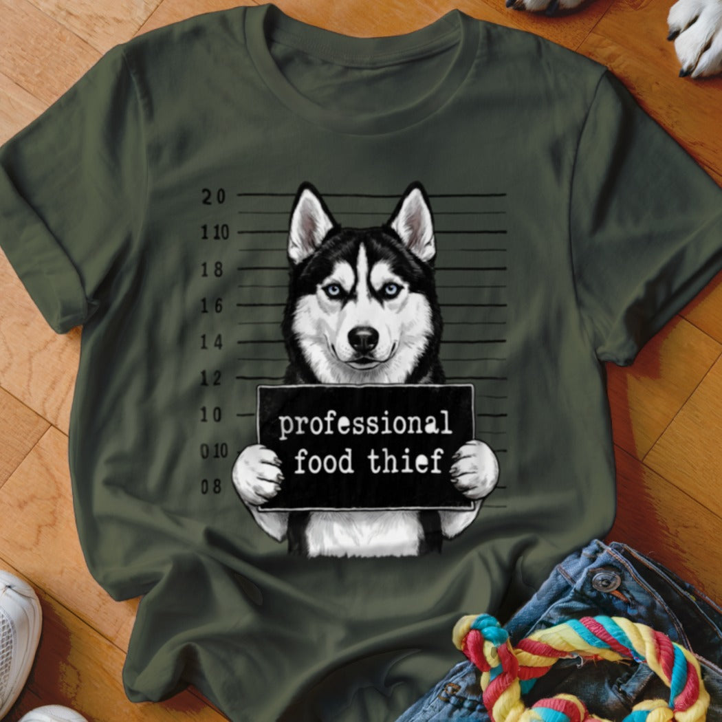 Husky mugshot with "professional food thief" sign on a dark green t-shirt.