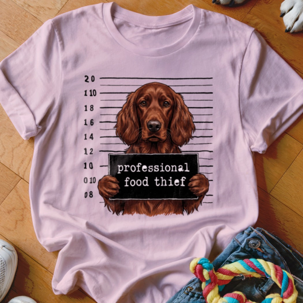 Irish setter mugshot with "professional food thief" sign on a pink t-shirt.