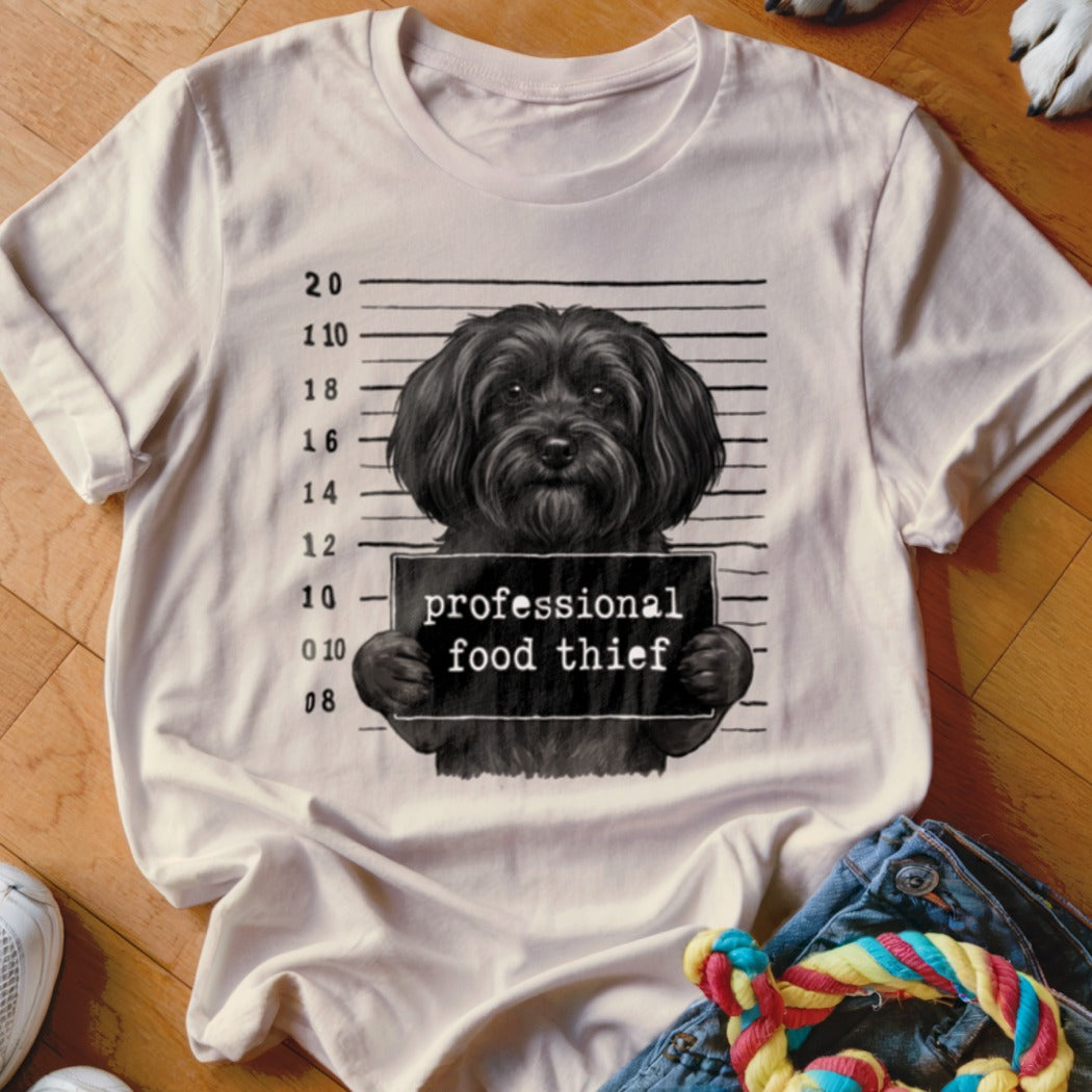 Black dog mugshot graphic with "professional food thief" text on a cream t-shirt.