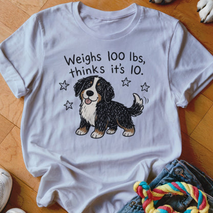 White t-shirt with cartoon Bernese Mountain Dog and text: Weighs 100 lbs, thinks it's 10.